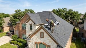 Roofer installing architectural shingles while roofing Round Rock home with limestone walls in Central Texas